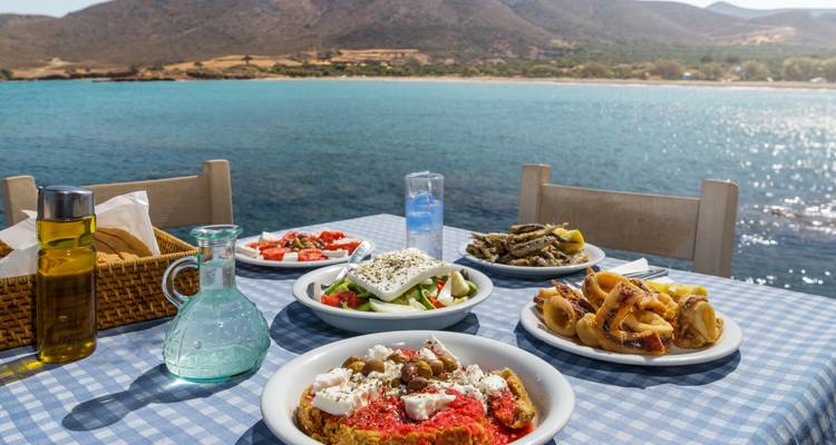 Plates of Greek food on a table with a seaside view.