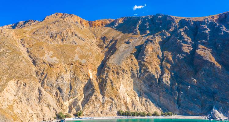 Rocky beach with towering cliffs under a clear blue sky.