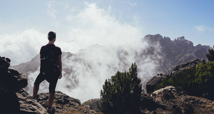Personne debout au bord d'une falaise avec des nuages environnants.