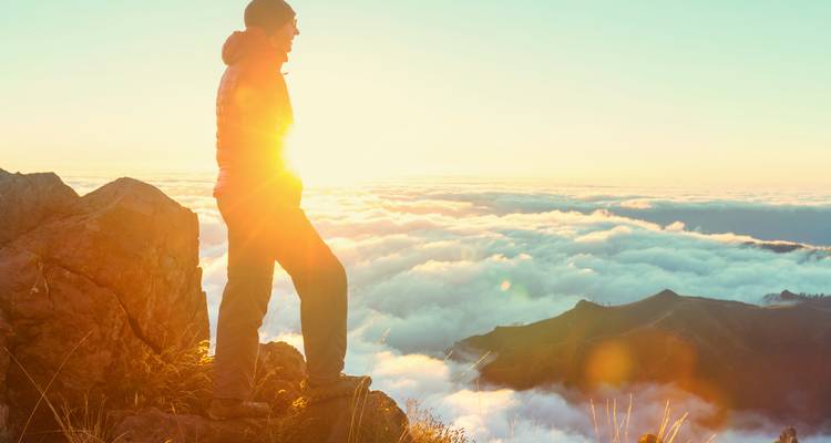 Silhouette d'une personne en veste contre un ciel de lever de soleil au-dessus d'un paysage nuageux.