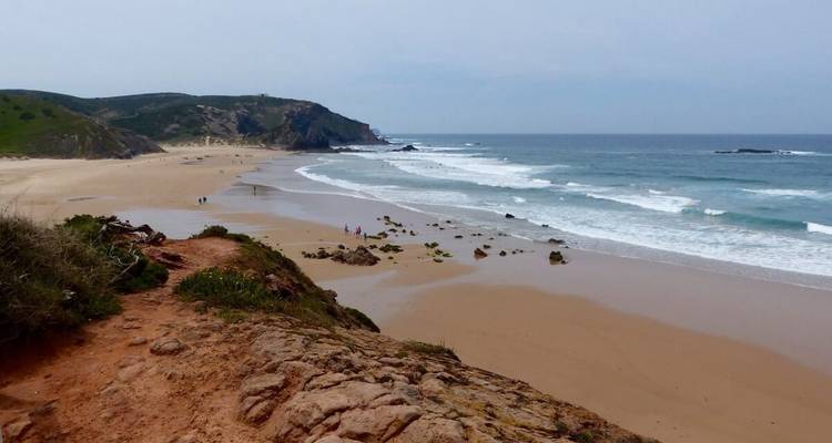 Sandstrand mit Wellen und schroffen Klippen in der Ferne.