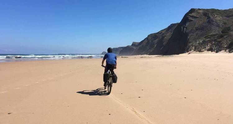 Radfahrer, der entlang eines weiten sandigen Strandes mit Wellen fährt.