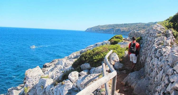 Une personne faisant de la randonnée le long d'un sentier côtier rocheux avec des eaux bleues.