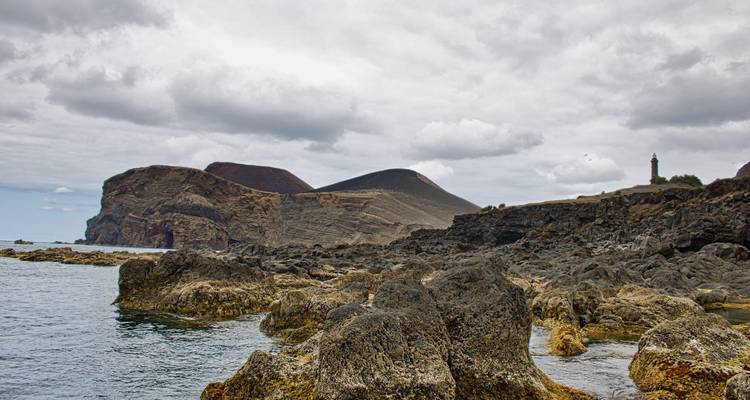 Rocky coastline with a lighthouse under a cloudy sky.