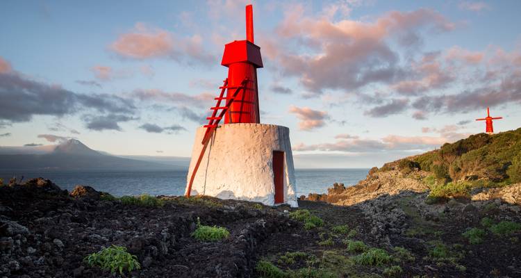 Lighthouse and red sculpture on a rocky coastline during sunset.
