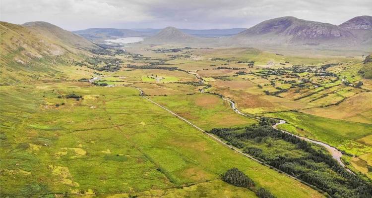 Vaste vallée de champs en damier et de rivières sinueuses avec des montagnes lointaines.