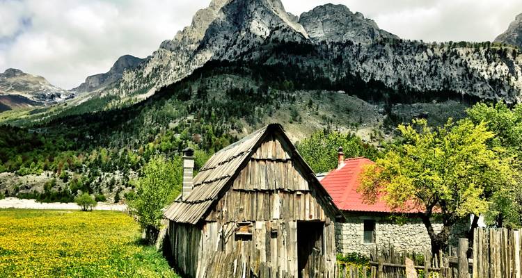 Rustikale Holz- und Steingebäude vor einer Kulisse schroffer Berge.
