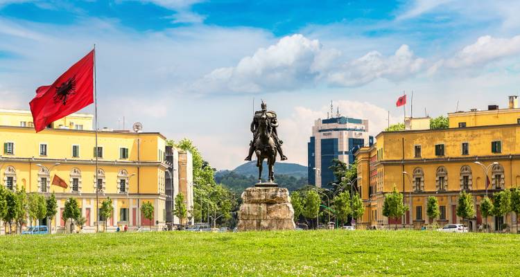 Eine Statue eines Reiters auf einem Platz mit Flaggen und Gebäuden im Hintergrund.