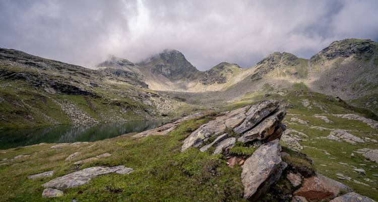 Eine neblige Berglandschaft mit Felsen und einem kleinen See.