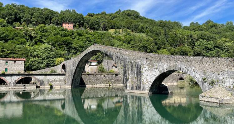 Eine steinerne Bogenbrücke mit Spiegelungen über einem ruhigen Fluss.