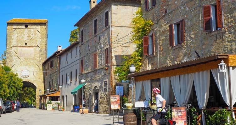 Een fietser trapt voorbij stenen gebouwen en middeleeuwse bogen in een charmante straat van een Umbrisch dorp.