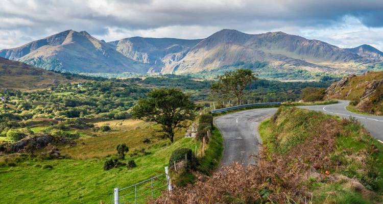 Een slingerende weg door een weelderig groene vallei omringd door bergen.