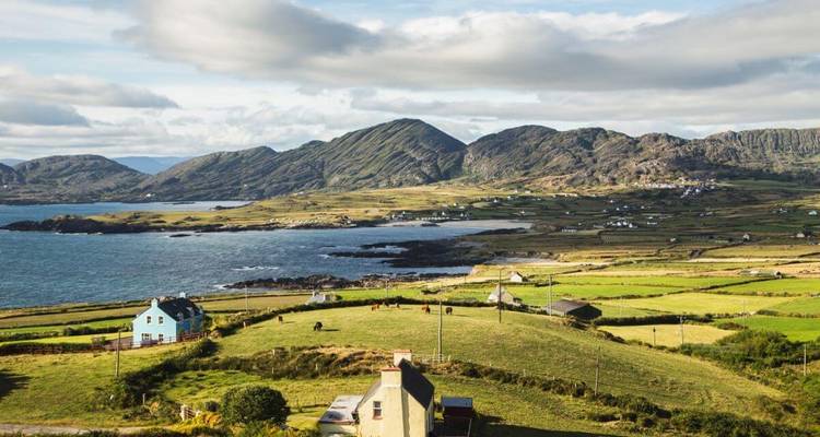 Een kustlandschap met velden en huizen, en heuvels in de verte.