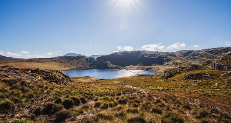 Een adembenemend uitzicht op een meer omringd door bergen met de zon erboven.