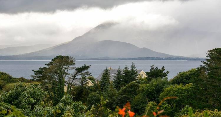 Een bewolkt uitzicht op de bergen over een huis en bomen.
