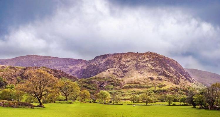 Een breed landschapsuitzicht met weelderige groene velden en bewolkte luchten.