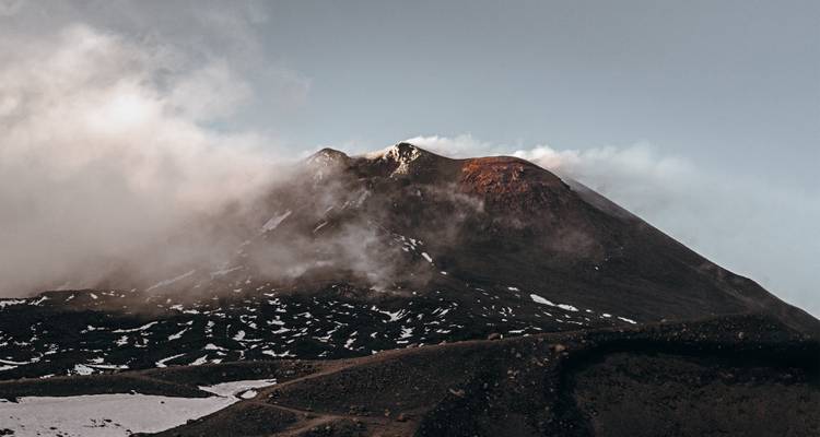 Un sommet de montagne entouré de nuages, partiellement couvert de neige.