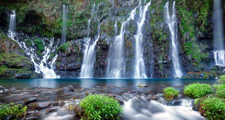 Belle cascade d'eau tombant dans un bassin bleu clair au cœur d'une jungle luxuriante.