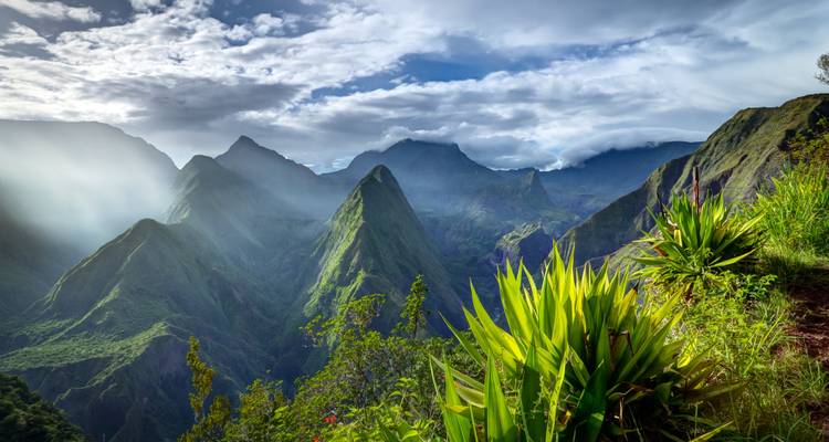 Des rayons de soleil filtrant à travers les nuages au-dessus d'une chaîne de montagnes déchiquetée.