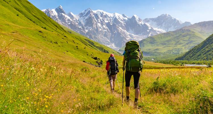Des randonneurs avec des sacs à dos marchant vers des montagnes enneigées.