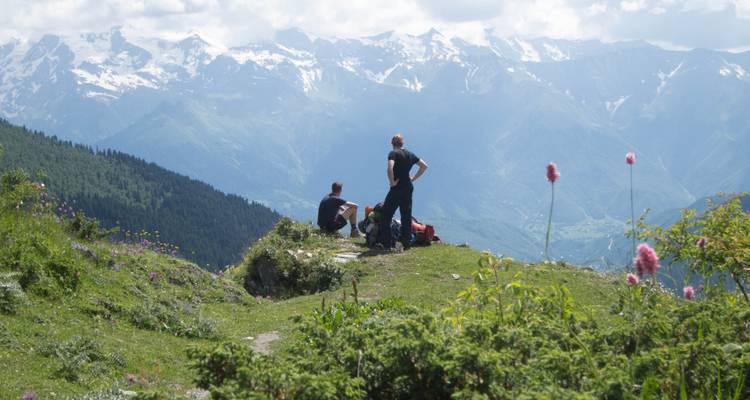 Randonneurs se reposant sur une butte herbeuse avec vue sur les montagnes enneigées.