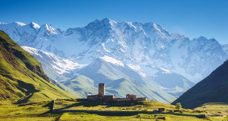 Mountain landscape with snow-covered peaks and a stone tower in the foreground.