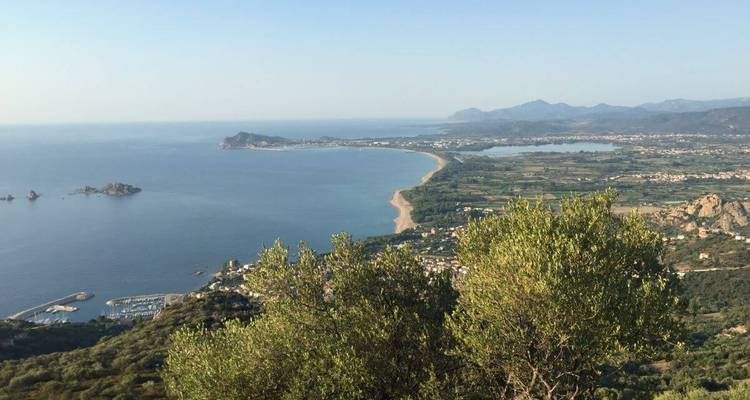 Panoramablick über eine breite Bucht, Sandstrand und fruchtbare Ebene mit entfernten Bergen im Hintergrund.