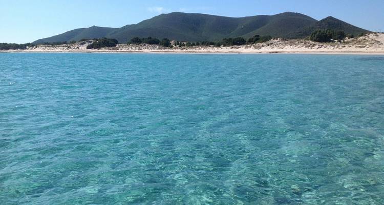 Eau bleue claire avec plage de sable lointaine et collines vertes.