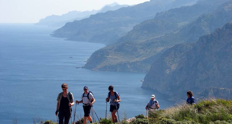 Groupe de randonneurs marchant le long d'un sentier de montagne côtier avec vue sur la mer.
