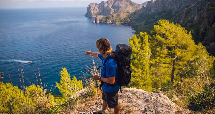 Randonneur pointant vers la mer depuis un sentier de montagne boisé.