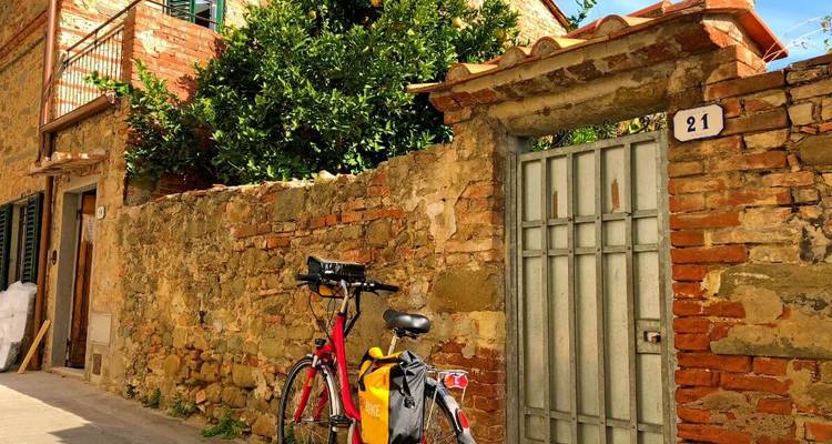 Ruelle pavée de pierre avec mur rustique, arbre feuillu et un vélo de tourisme rouge appuyé contre un portail usé par le temps numéroté 21.