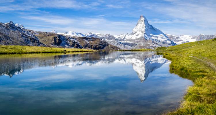 Reflet du Cervin dans un lac calme avec paysage montagneux.