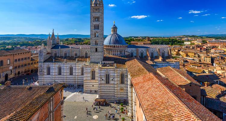 Vista detallada de la fachada de mármol rayado de la catedral de Siena y su campanario que domina los tejados de la ciudad circundante.