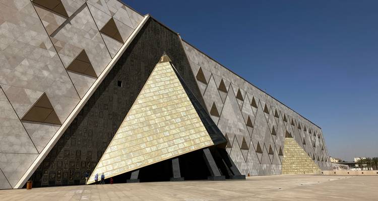 Façade angulaire moderne du Grand Musée égyptien avec entrée triangulaire sous un ciel dégagé.