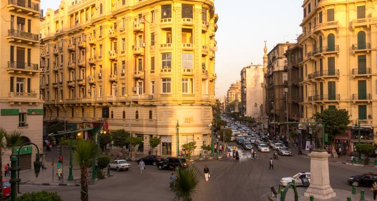 La lumière dorée du soleil baigne des bâtiments coloniaux ornés qui surplombent un carrefour animé du Caire rempli de circulation.
