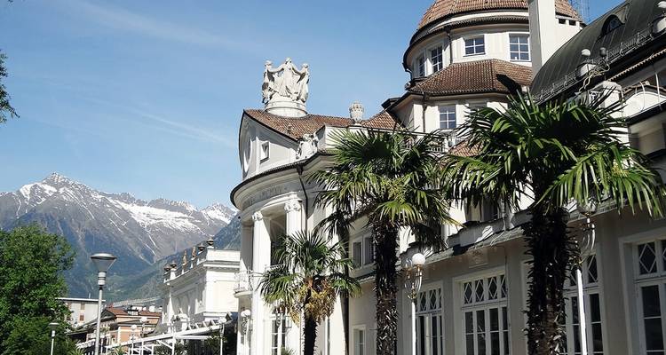 Elegante edificio con palmeras y picos nevados distantes.