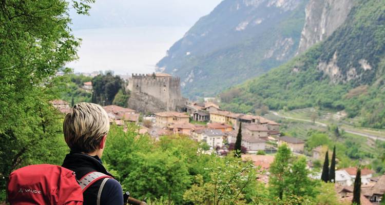 Person mit einem roten Rucksack, die ein Tal und eine Burg überblickt.