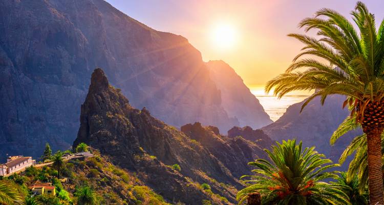 Coucher de soleil sur des montagnes escarpées et des palmiers.
