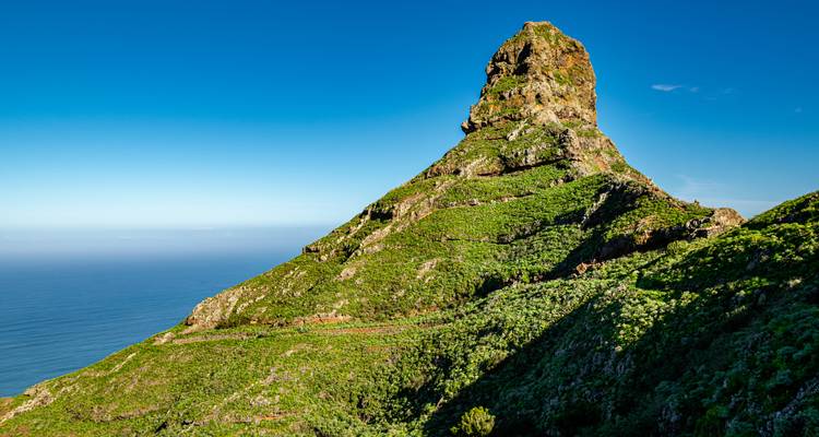 Formation montagneuse unique avec un terrain verdoyant luxuriant et un ciel bleu clair.