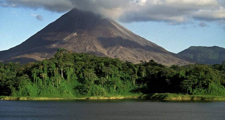 Volcan avec des nuages au-dessus du sommet entouré de forêt.