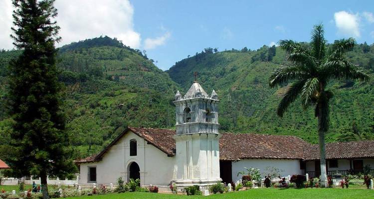 Église rustique avec un clocher au milieu de collines verdoyantes.