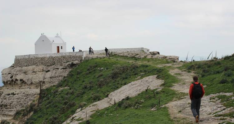 Chapelle blanche sur une colline avec des gens qui marchent et font du vélo à proximité.
