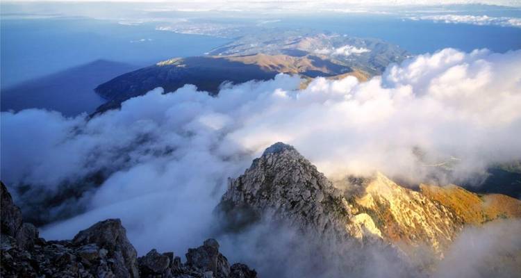Chaîne de montagnes avec des nuages et la mer visible d'en haut.