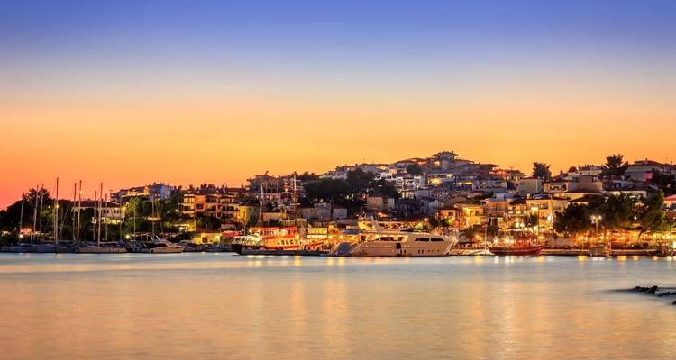 Village côtier illuminé au coucher du soleil avec des bateaux sur l'eau calme.