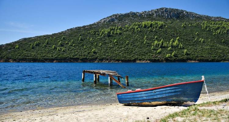 Un petit bateau sur une plage avec une eau bleue claire and un ponton en bois.