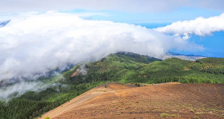 Vista sobre colinas verdes cubiertas de nubes con océano de fondo.