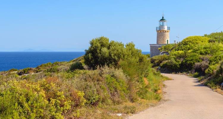 Scène côtière ensoleillée avec un phare et un sentier.