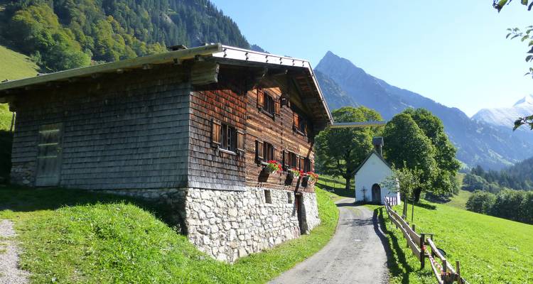 Houten huis en pad in bergachtig landschap.