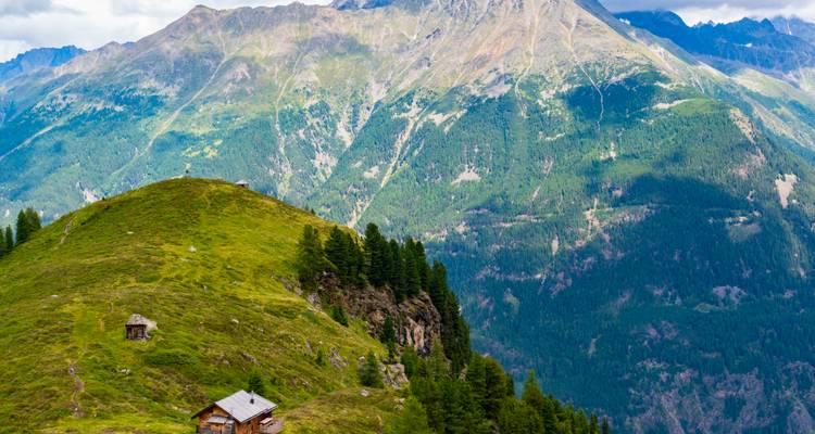 Alpine Landschaft mit sanften Hügeln und Hütten.