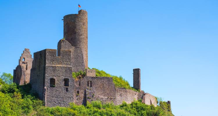 Alte Burgruinen auf einem Hügel mit klarem blauen Himmel.